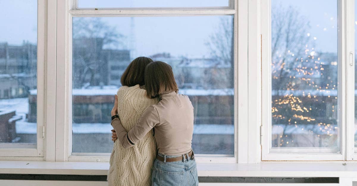 Two people hugging in front of a window