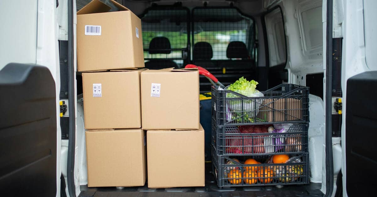 Back of a van with five brown boxes and crates of produce