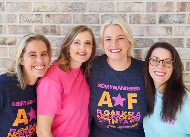 Four people posing in front of a light tan brick wall