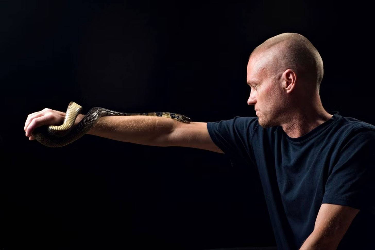 A man in a navy shirt with a snake slithering up his arm
