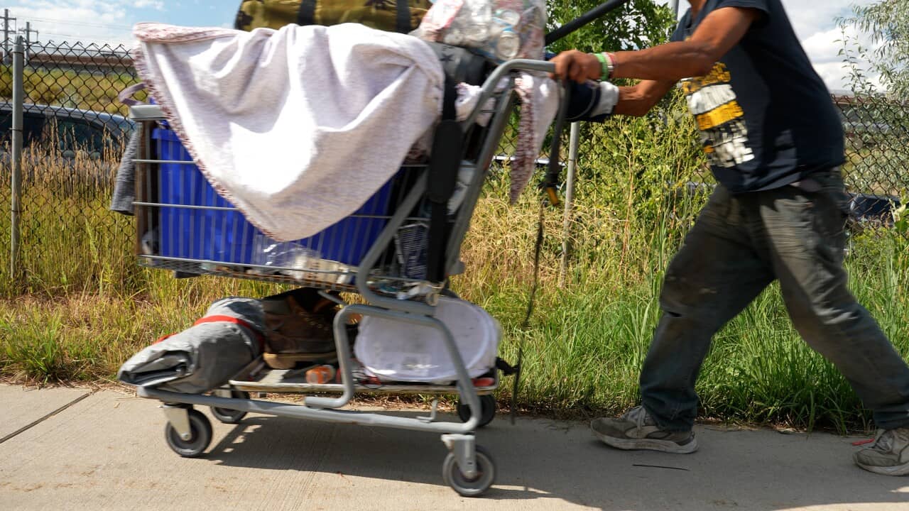 A person pushing a shopping cart filled with blankets, shoes, and other items