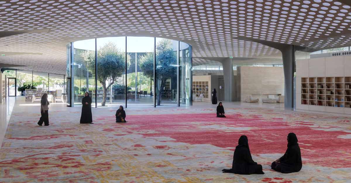 Women in black robes scattered in the middle of a large room, a red yellow and grey rug is in the middle of the floor