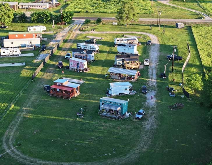 Birds-eye view of a group of about 15 tiny homes and RVs in a grassy area