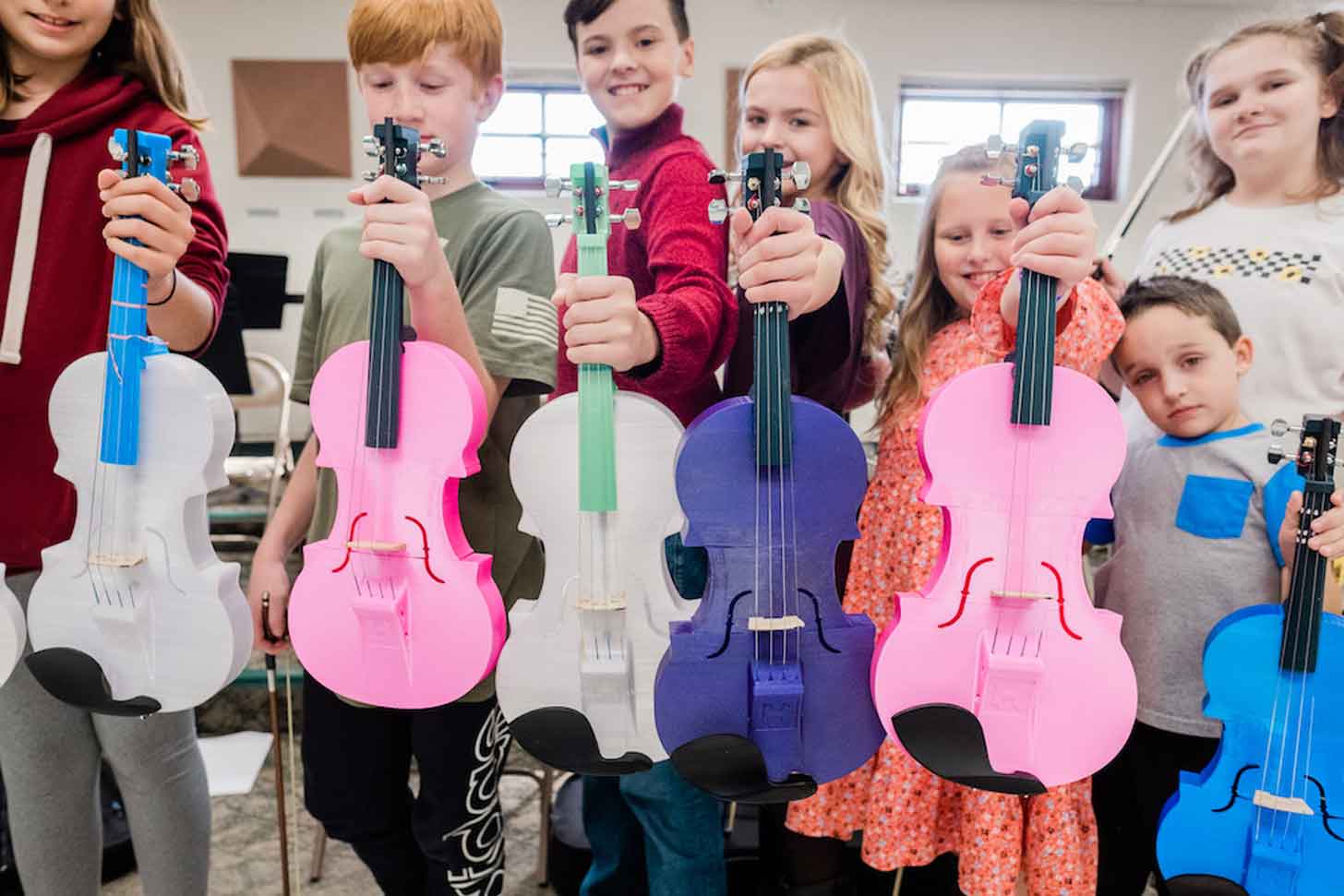 Students holding multi-colored violins in purple, blue, pink, and white.