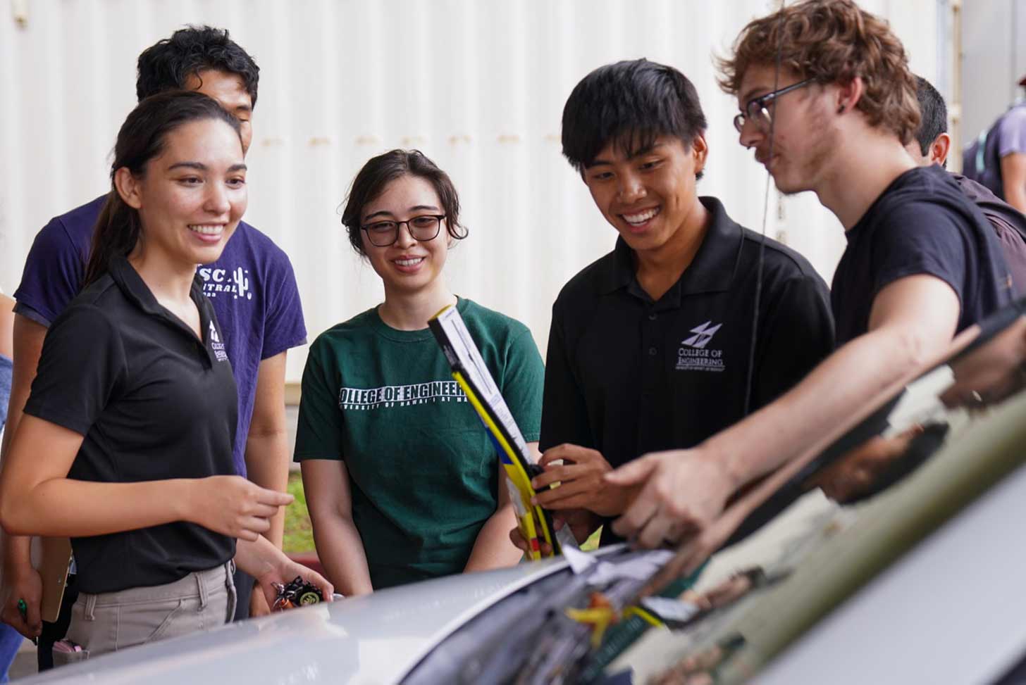Six students around the hood of a car