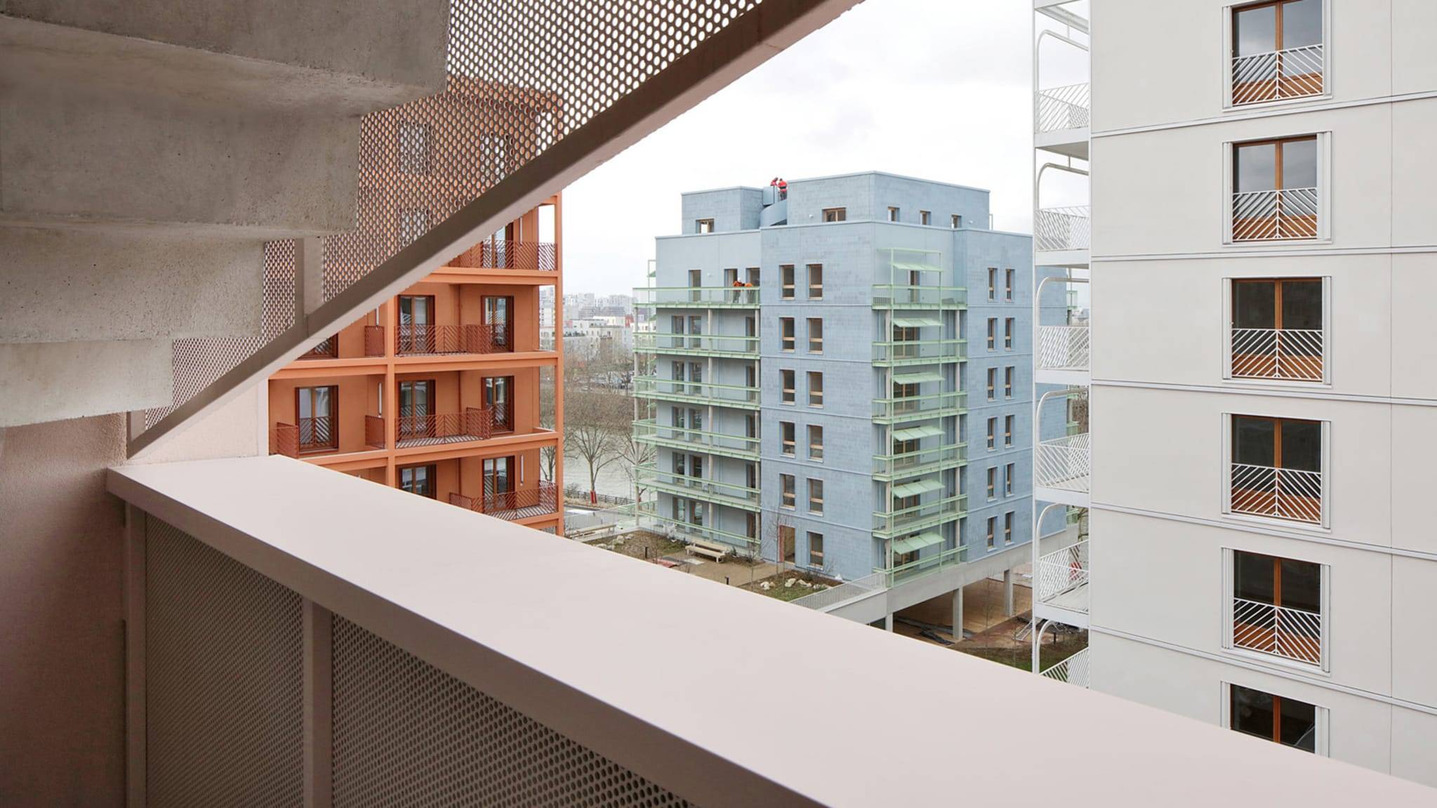 View of three multi-story buildings from a nearby staircase: one is orange, one is light blue and green, and the third is white.