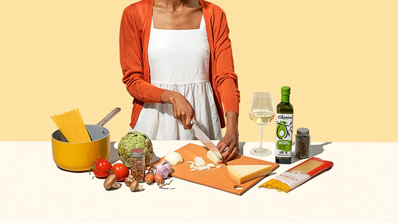 A person cutting an onion on a cutting board with food items around them