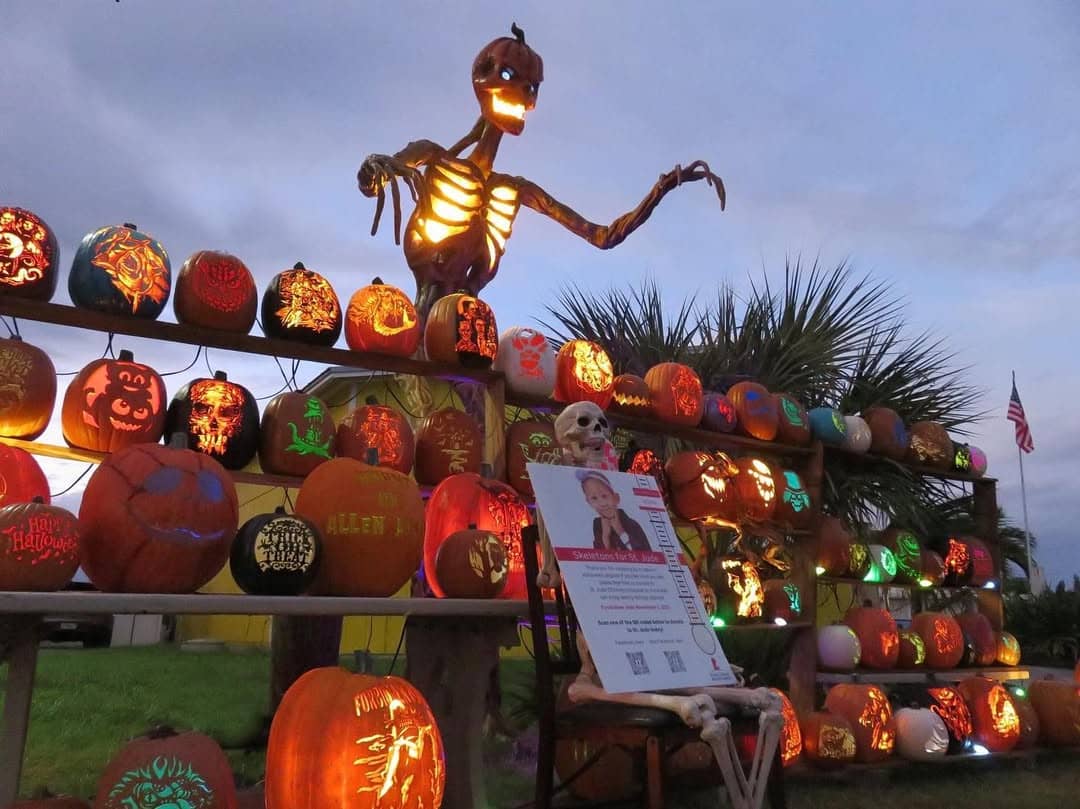 Large lit up skeleton towering over shelves filled with carved pumpkins