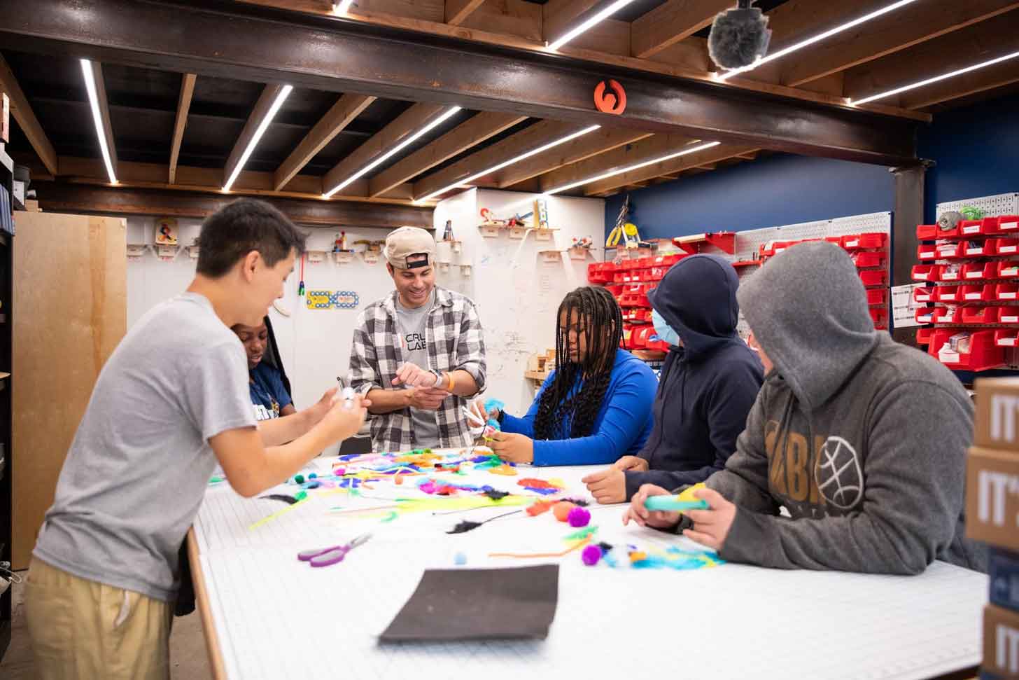 Mark Rober and five students around a table with colorful materials on top of the table