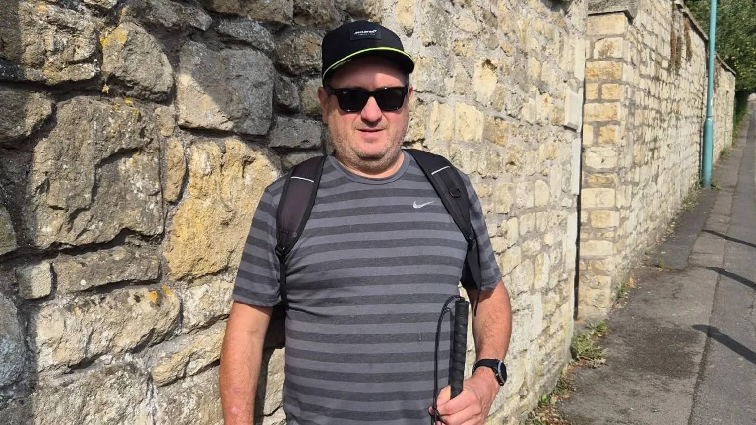Andy Evans wearing black sunglasses, a hat, and holding a walking cane