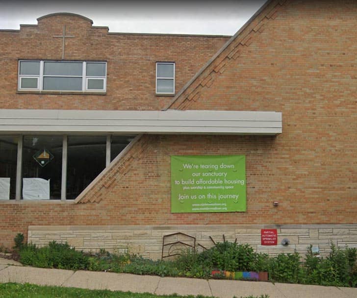 Exterior of a brick building with a green sign that says "We're tearing down our sanctuary to build affordable housing"