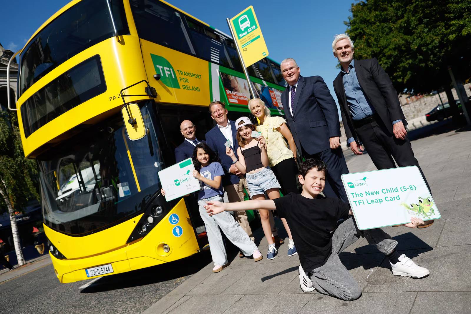 A group of adults and children in front of a yellow double-decker bus