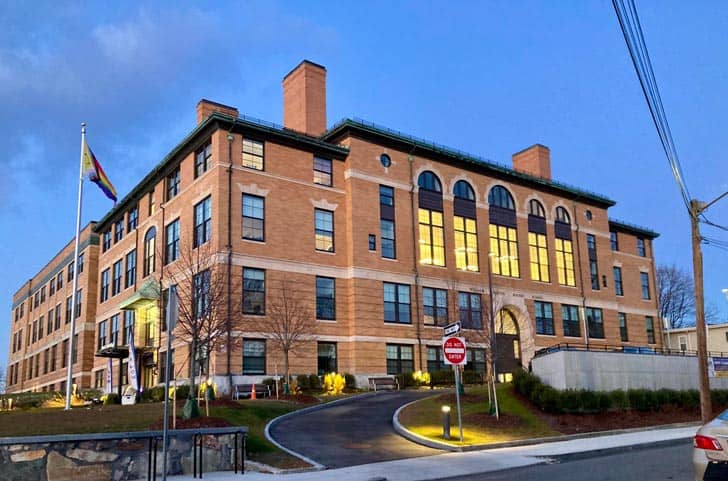Exterior of a multi-story red-brick school building, with a pride flag on a flagpole outside