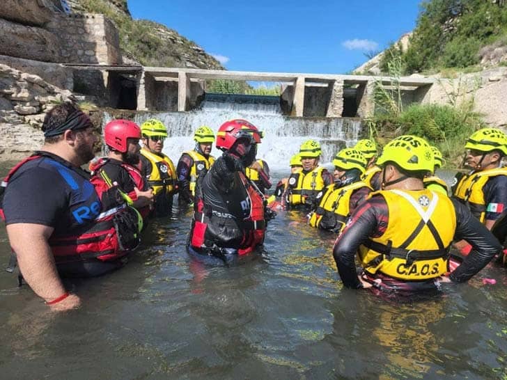 People in yellow life jackets standing in waist-deep water