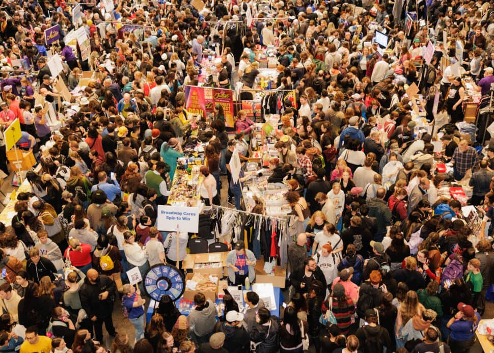 Overhead view of a crowded indoor event with hundreds of people walking among vendor booths and tables displaying merchandise and clothing.