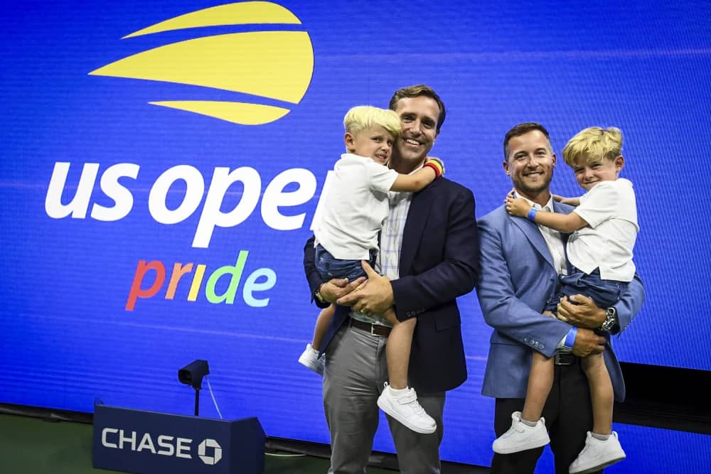 Brian Vahaly, his husband, and their two children in front of a "US Ope Pride" background