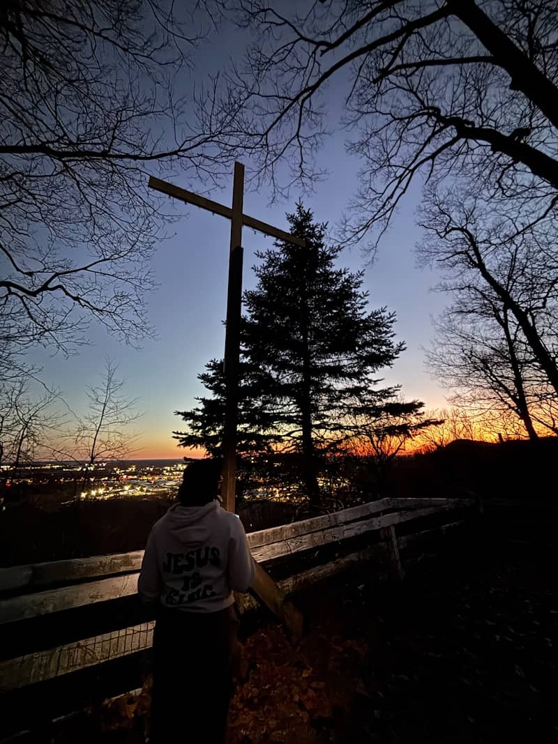 Person looking at a cross at sunset