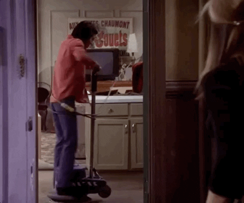 Monica, from Friends, standing on a floor polisher that's going in circles
