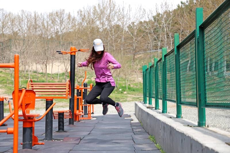 Woman jumps happily near exercise equipment.