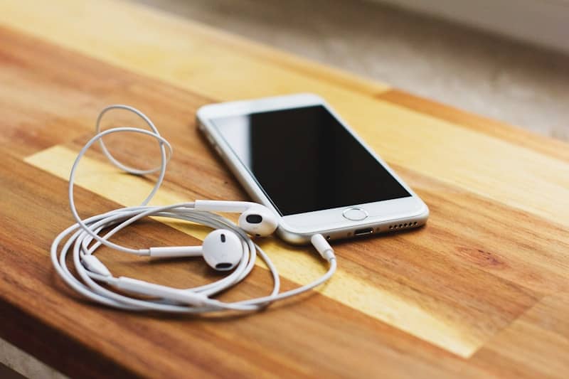 silver iPhone 6 with EarPods on brown wooden table