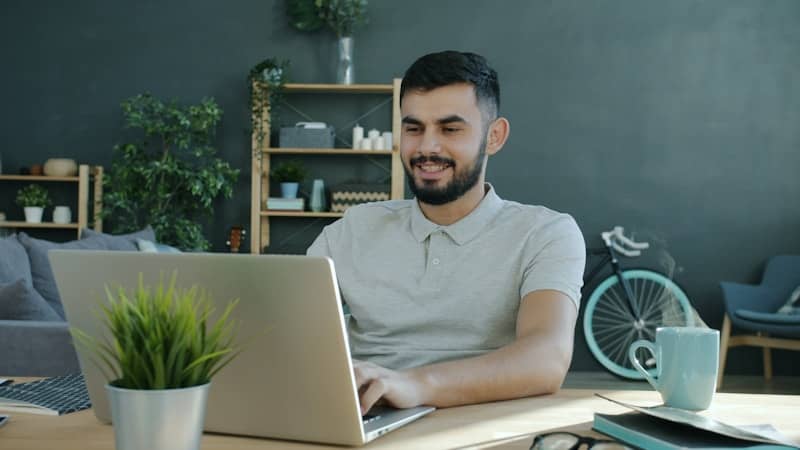 Man smiling while working on a laptop at a desk.