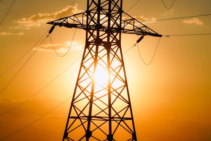 An electric tower stands silhouetted against the sunset.
