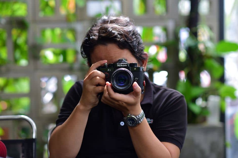 Adult photographing with a Nikon camera amidst a green outdoor setting, capturing creativity.