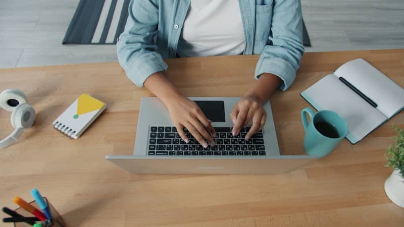 Person typing on a laptop at a wooden desk.