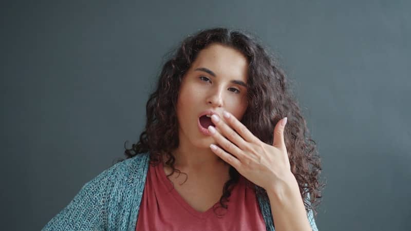 A young woman yawning with her hand over her mouth.