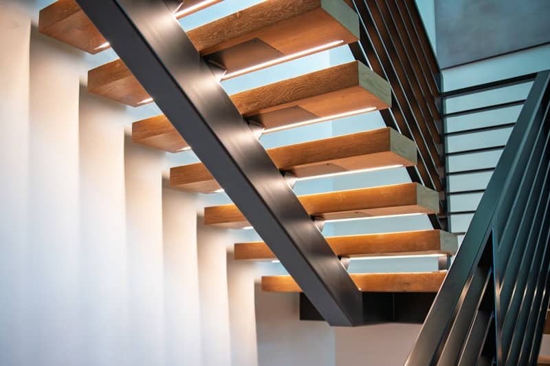 Modern wooden staircase with metal railings and lighting.
