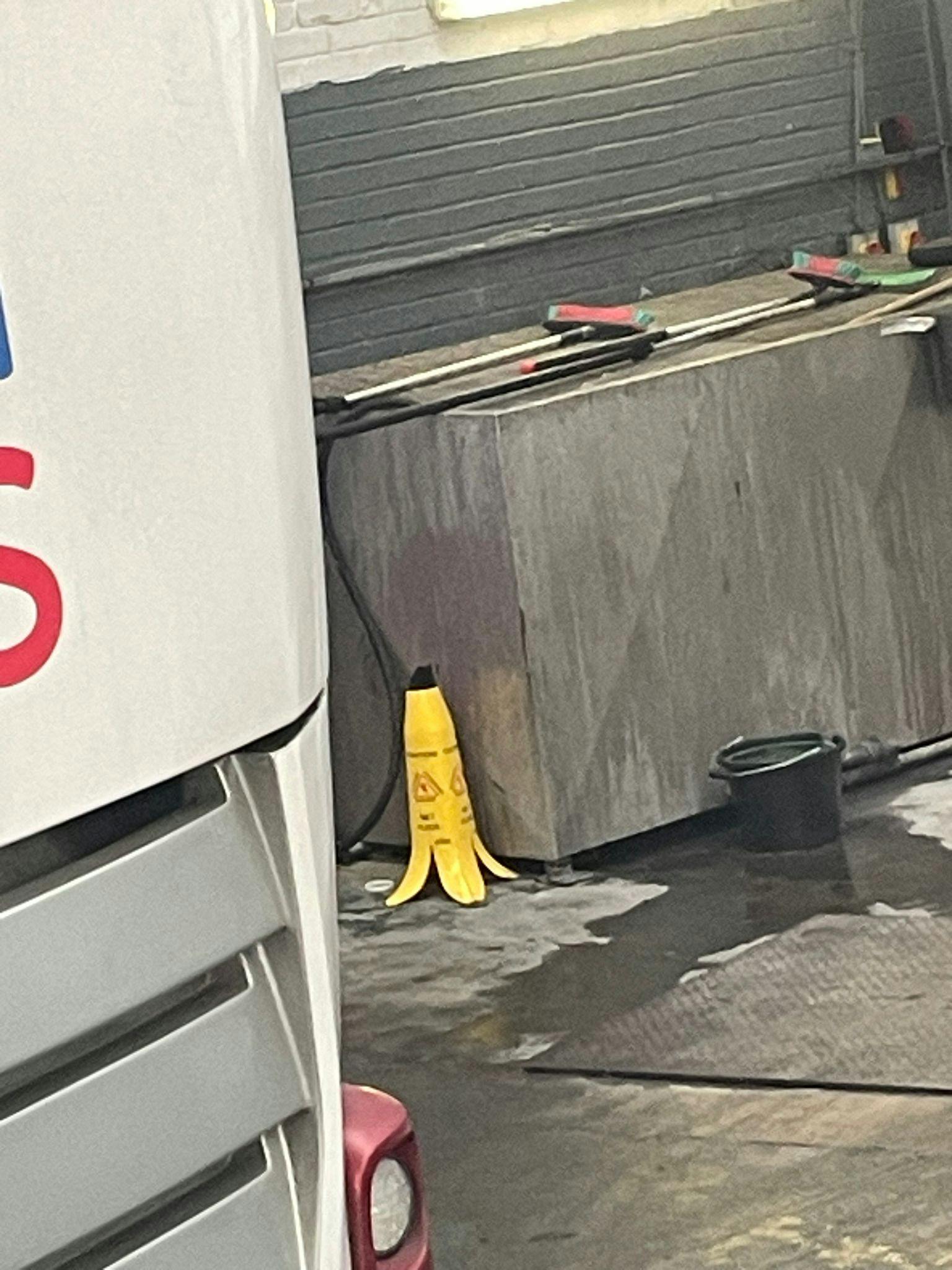 Photograph of a room with a water spillage on the floor. Next to the spillage, a "wet floor" warning sign in the shape of a banana.