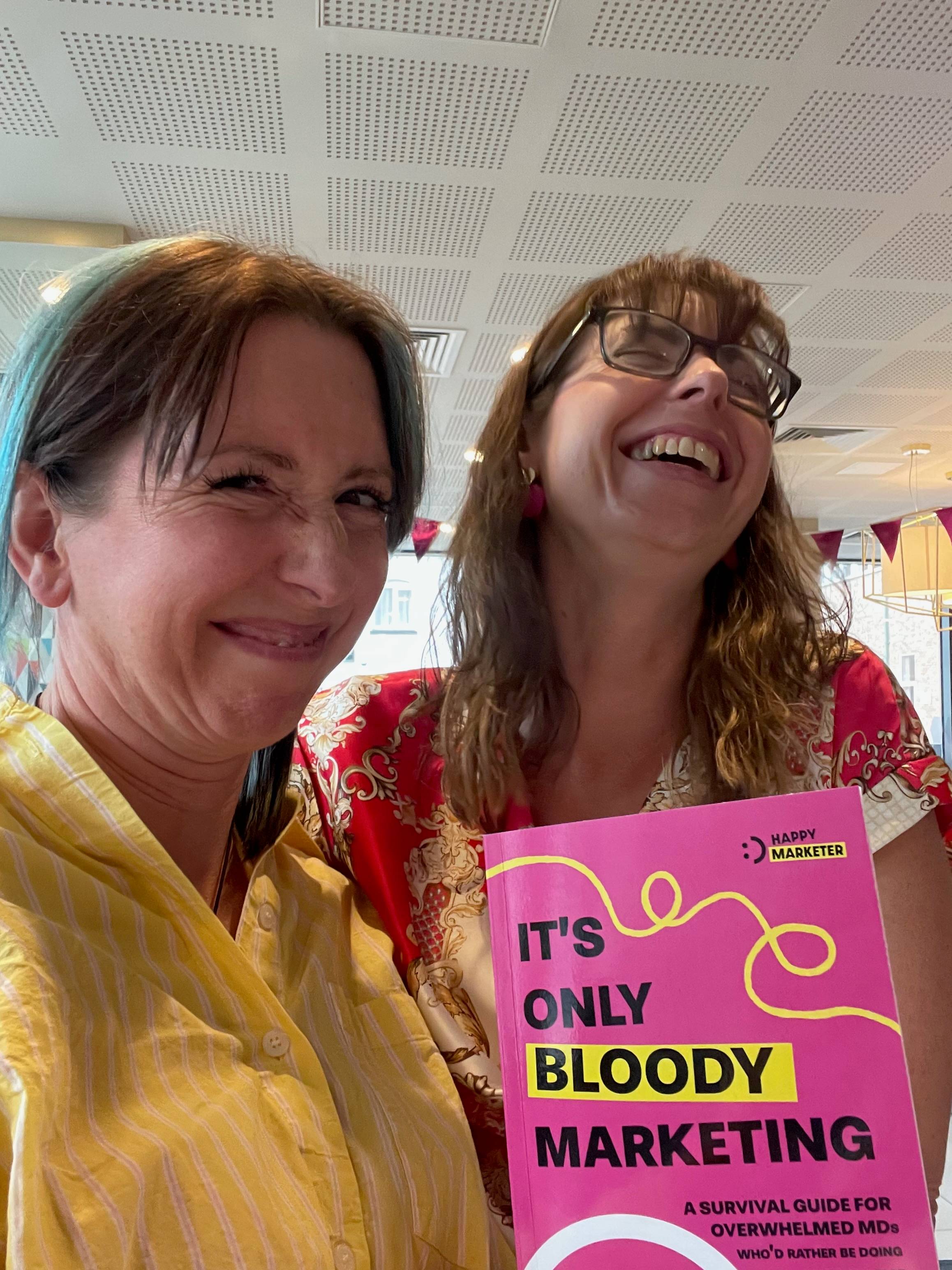 Vicky and Sophie are two white women looking… well, delighted in Sophie’s case and a bit fucking weird in Vicky’s. Vicky is scrunching up her eyes and grinning with mouth closed, and giving herself many chins. She wears a yellow and white striped shirt th
