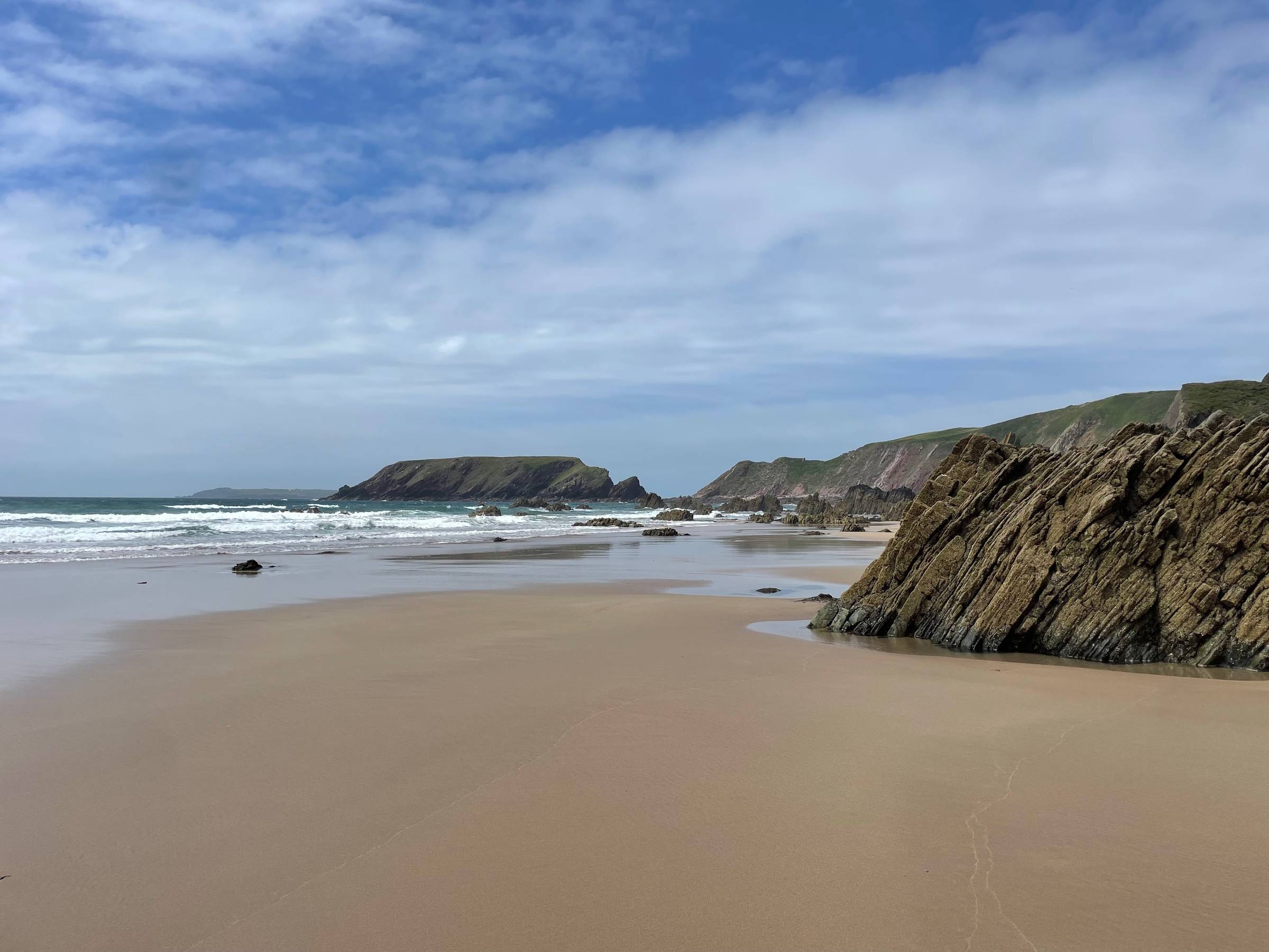 A deserted beach with the tide out. Golden sands, scattered rocks, and glorious rock formations hiding the best rock pools. In the distance, an island that is only an island at high tide.
