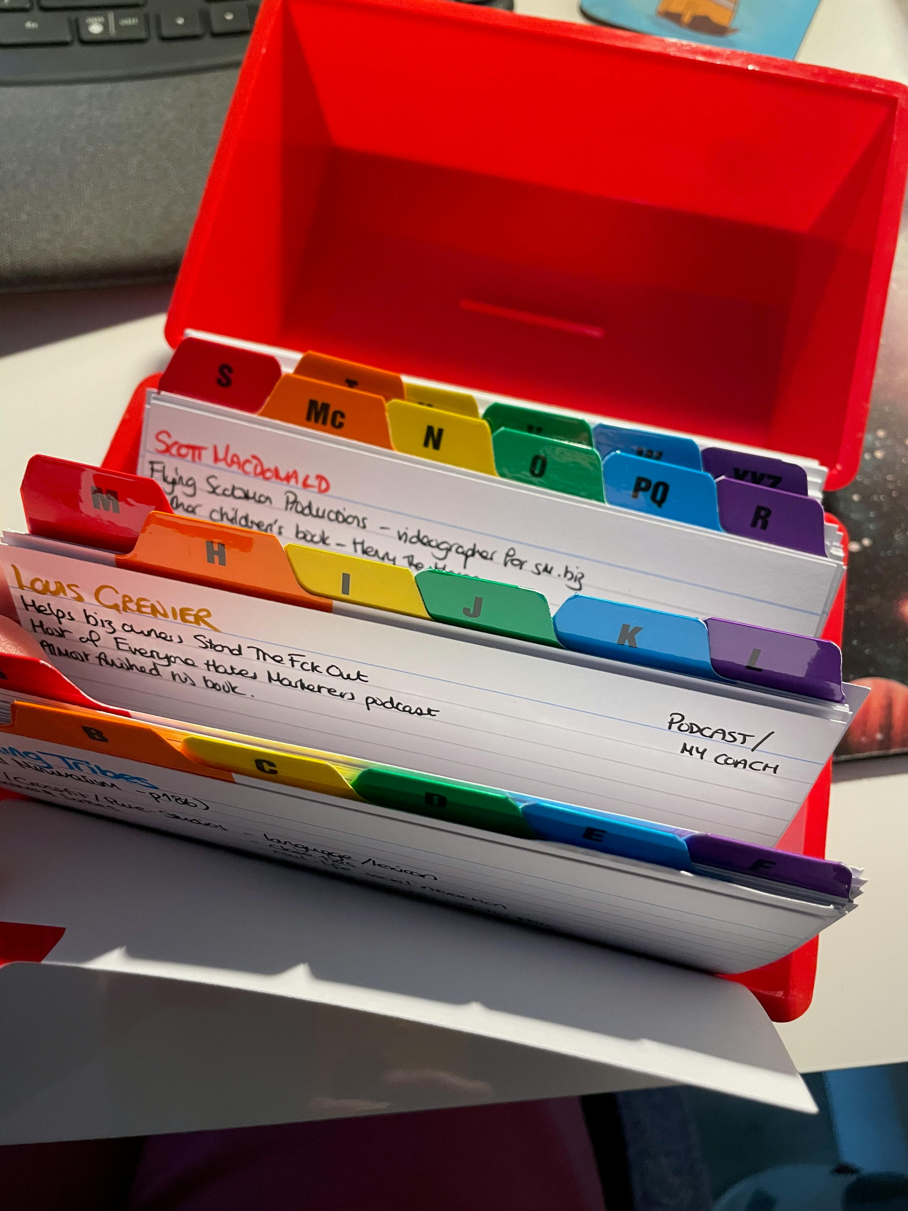 Red index card box open to show alphabet dividers and snippets of 2 cards — Stuart MacDonald and Louis Grenier