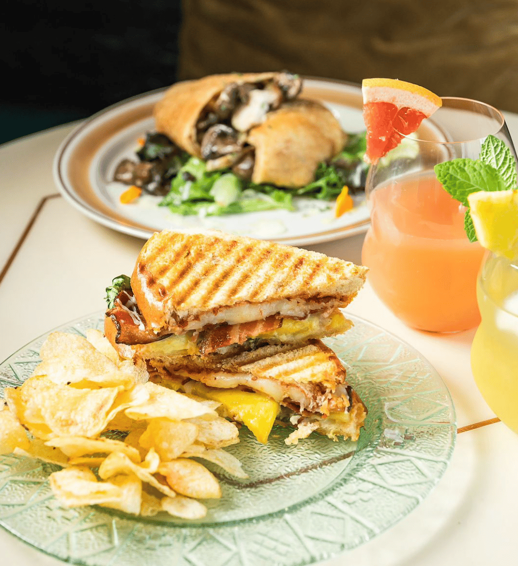 A close up photo of a toasted sandwich with chips and drinks and another meal in the background