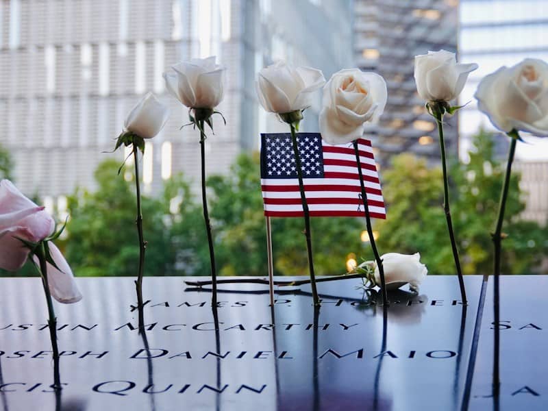 White roses and a small American flag placed on a memorial wall with engraved names