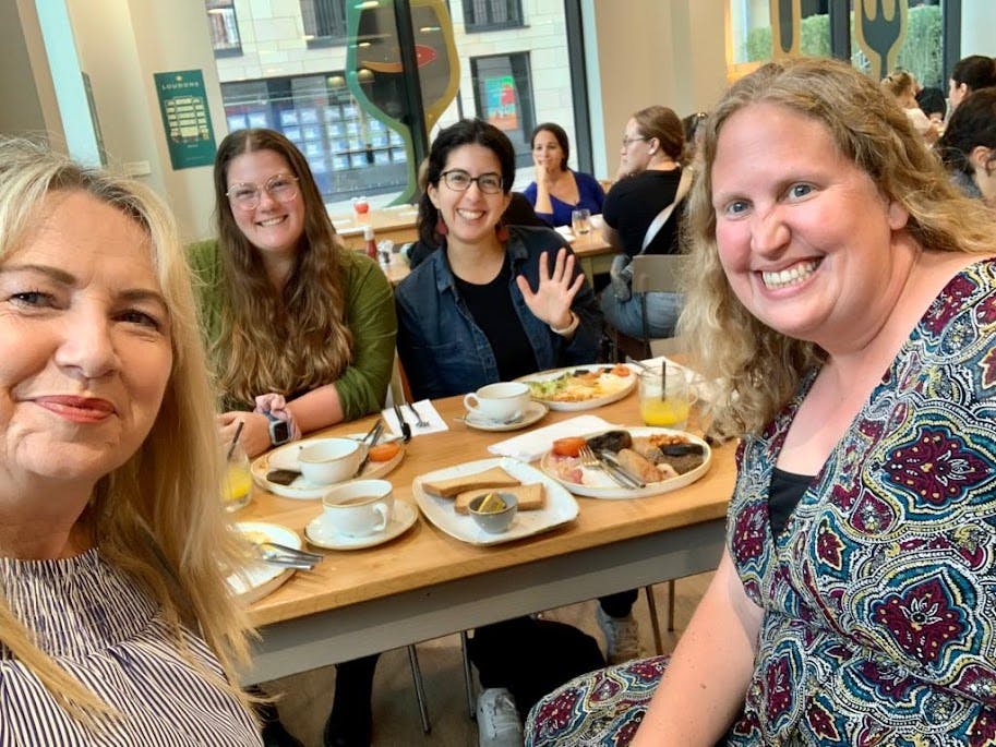 Four Wanderful Members smile at the camera while seated around a table with Full Scottish Breakfast plates and cups of coffee