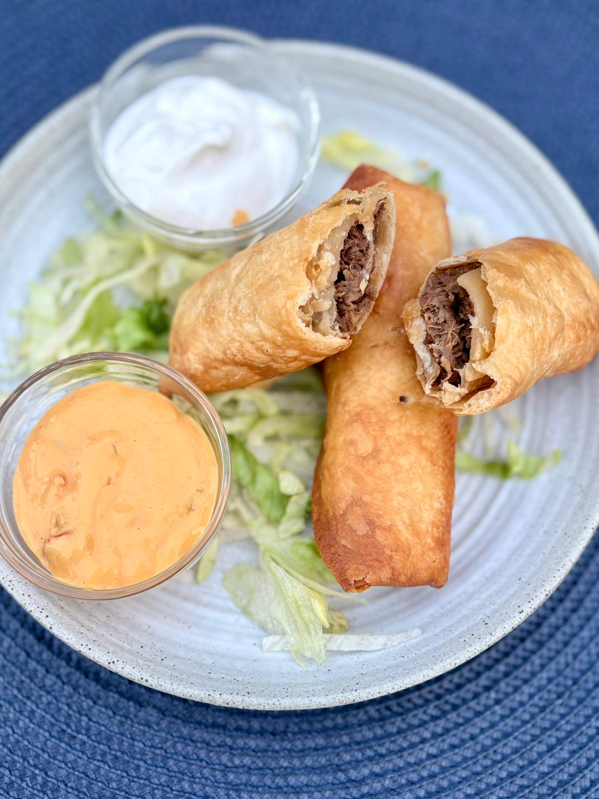 shredded beef flautas on a bed of lettuce with small bowls of queso and sour cream on a plate