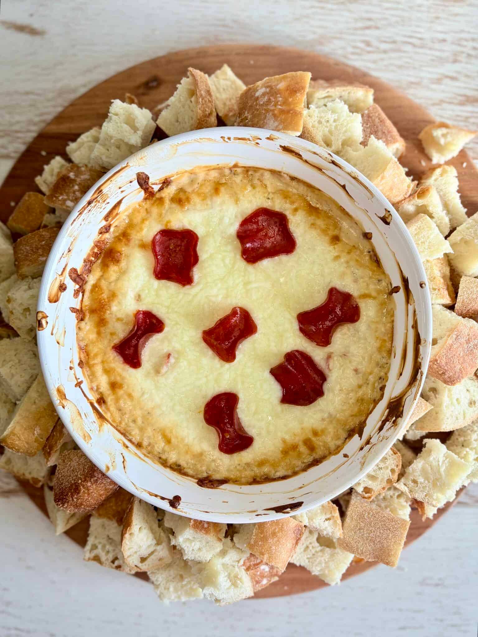 hot pizza dip topped with pepperoni in a white bowl surrounded by chunks of bread