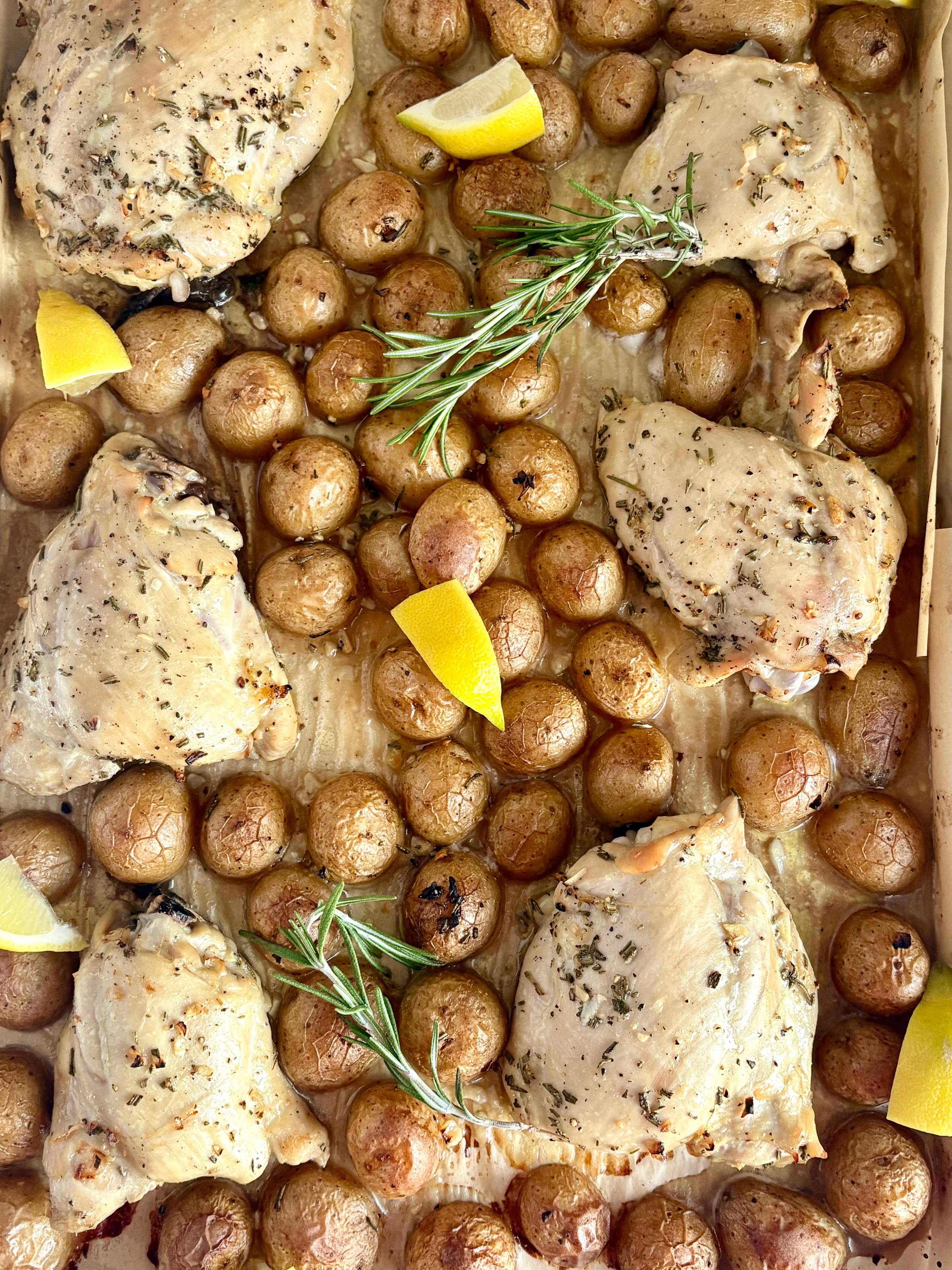 chicken thighs on a sheet pan with potatoes, lemon wedges and fresh rosemary