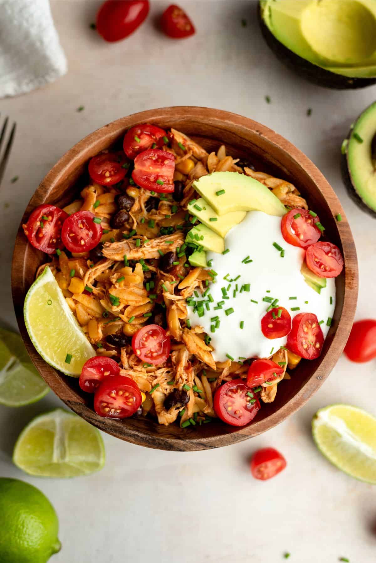 A bowl of chicken enchilada pasta with sour cream, tomatoes, avacado, and chopped tomatoes with a slice of fresh lime