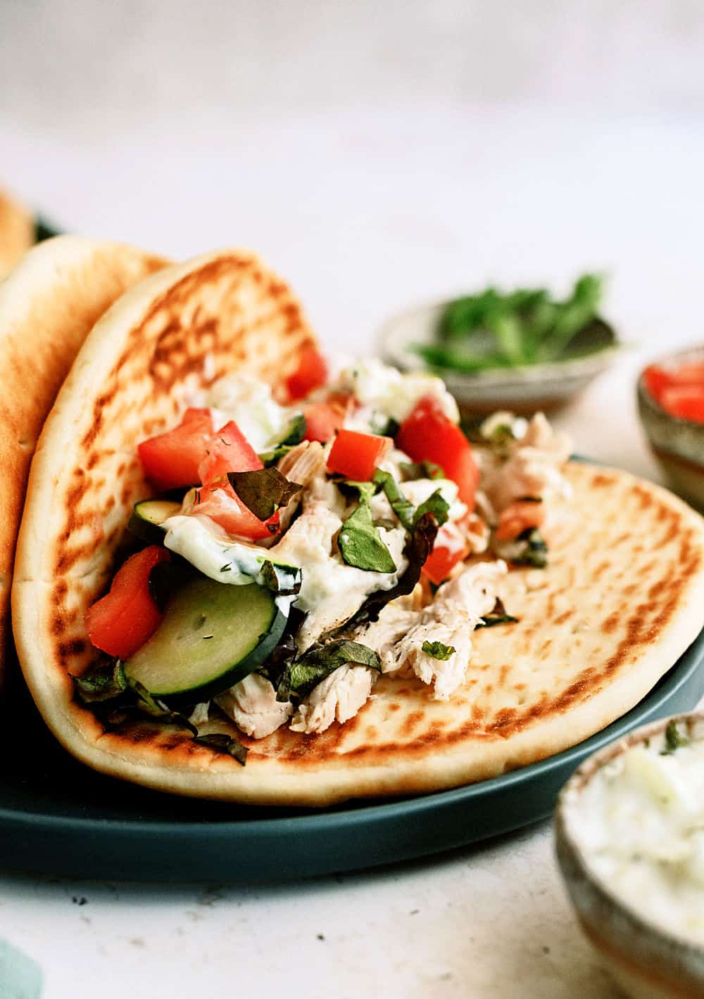 Slow cooker chicken on a pita topped with tzatziki, tomatoes, and cucumbers