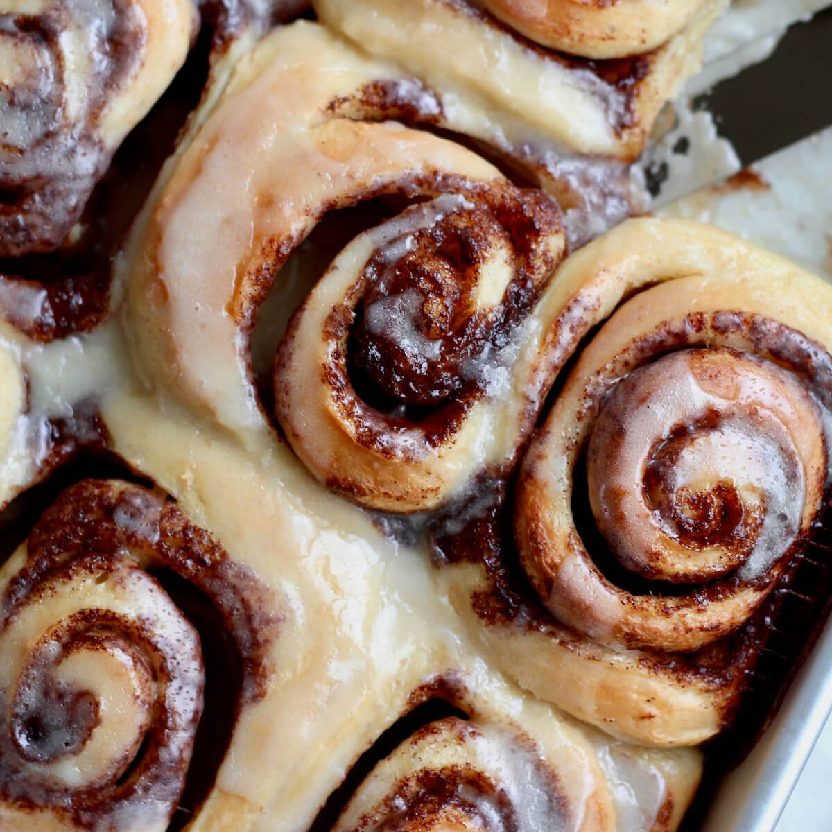 Sourdough cinnamon rolls covered in icing in a baking dish.