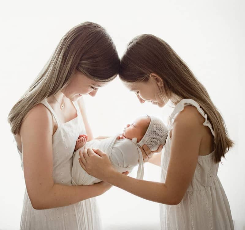 Sweet sibling moment: big sisters snuggling their newborn sister