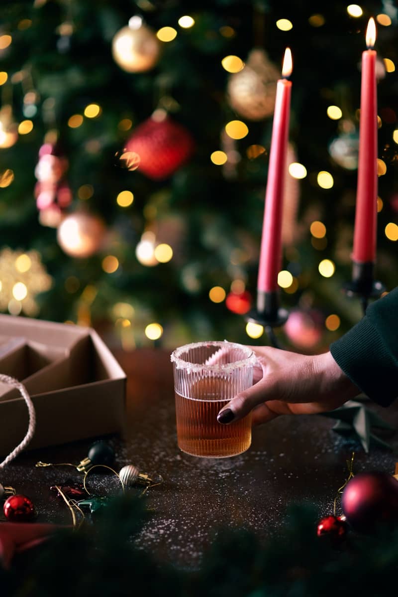 A person reaching for a drink in front of a christmas tree