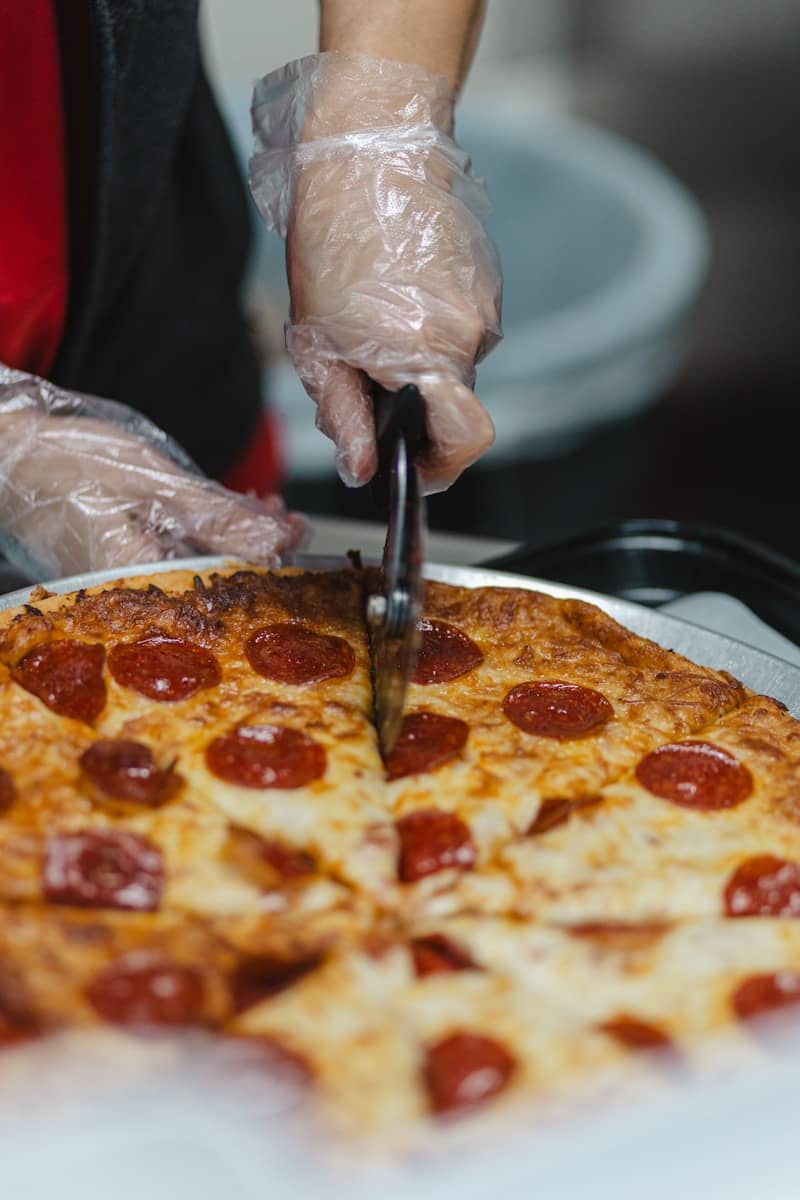Hands in gloves slicing a pepperoni pizza.