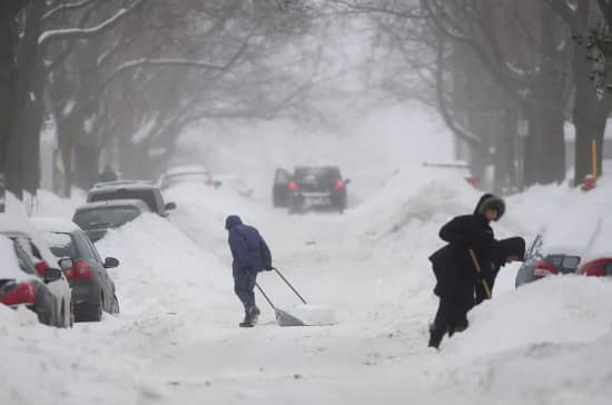 People attempting to dig their cars out of a deeply snow covered street.