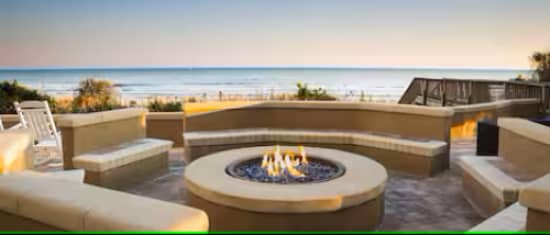 Possibly AI generated photograph of a fire pit and a beach in the background.