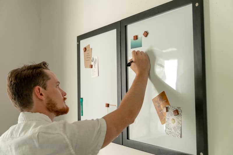 a man writing on a white board with sticky notes on it