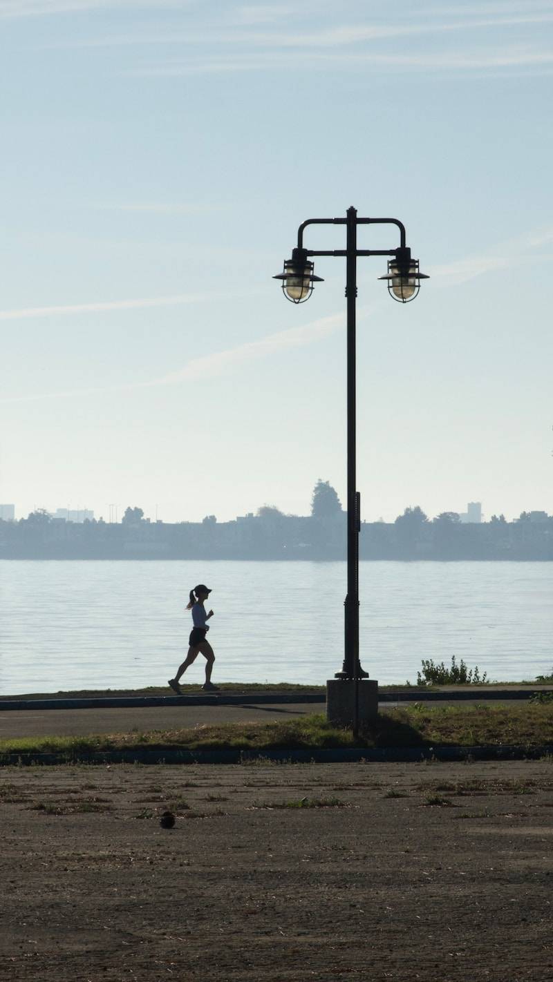 Woman jogging by the water near a lamppost